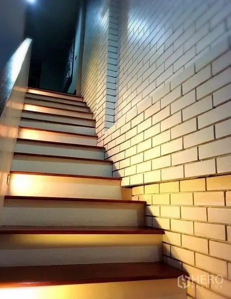 Townhouse for rent in Bang Rak, Bangkok - Wood staircase with step lighting beside a white brick accent wall in the townhouse.