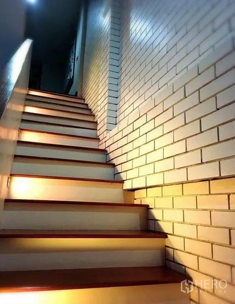 Townhouse for rent in Bang Rak, Bangkok - Wood staircase with step lighting beside a white brick accent wall in the townhouse.
