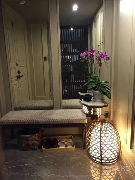 Condominium for sale in Pathum Wan, Bangkok - Entry foyer with bench seating, full-height mirror, orchid arrangement and woven floor lamp.