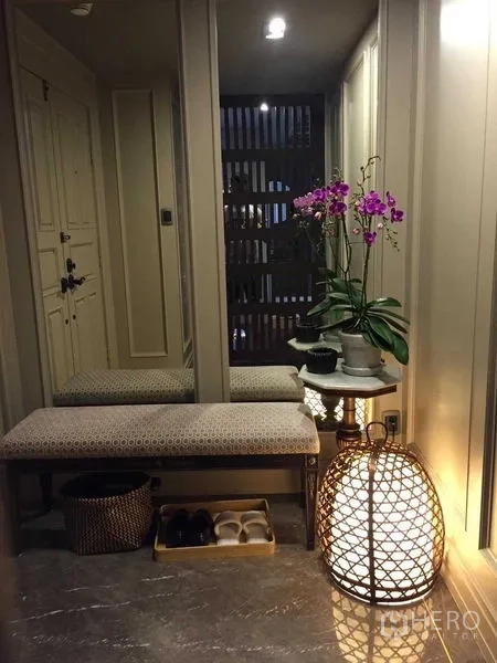 Condominium for sale in Pathum Wan, Bangkok - Entry foyer with bench seating, full-height mirror, orchid arrangement and woven floor lamp.