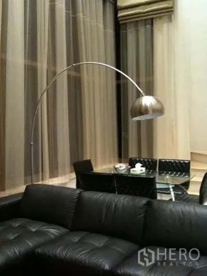 公寓 出租或出售在Khlong Toei, Bangkok - 挑高客厅，黑色真皮沙发、弧形落地灯与纱帘。