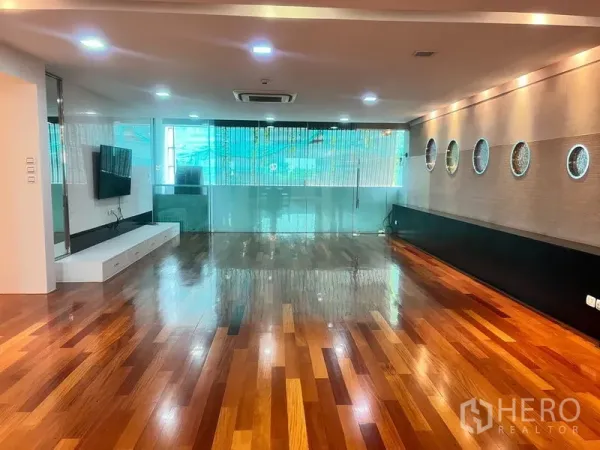 公寓 出租在Khlong Toei, Bangkok - 宽敞客厅，亮泽木地板、筒灯、电视墙与玻璃隔断。