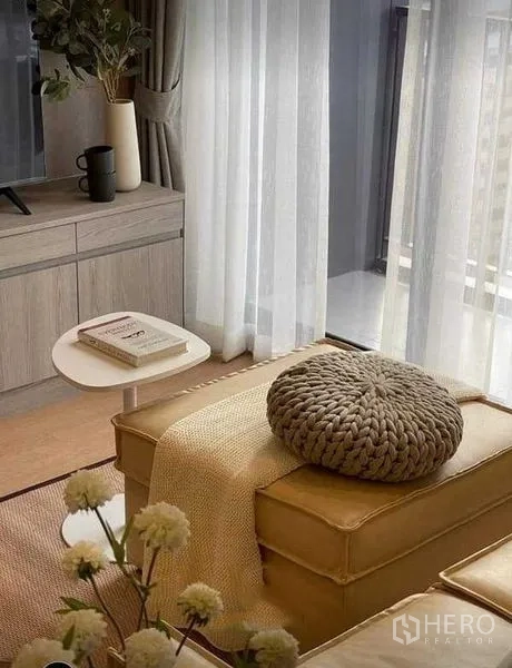 Condominium for rent in Watthana, Bangkok - Lounge by the balcony with ottoman, side table and sheer drapes framing a city skyline view.