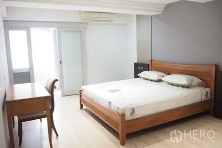 Condominium for rent in Pathum Wan, Bangkok - Spacious bedroom with wooden bed, desk and sliding door to the balcony.