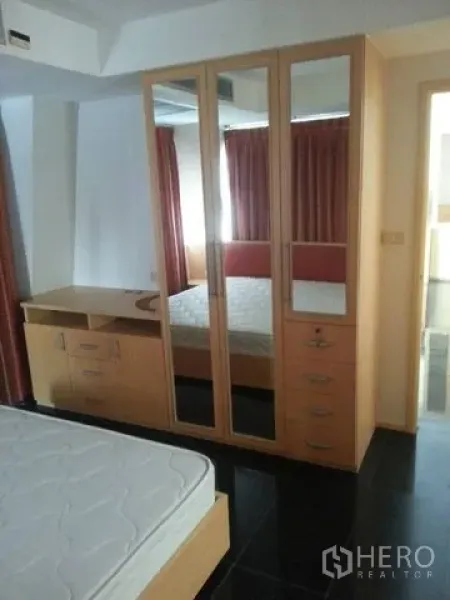 公寓 出租在Bang Rak, Bangkok - 卧室配有镜面衣柜、内置书桌与双人床，深色地砖与红色窗帘。