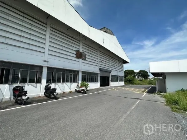 คลังสินค้า ให้เช่าในLam Luk Ka, Pathum Thani - อาคารโกดังสีขาวขนาดใหญ่ ด้านหน้าเป็นประตูโหลดดิ้ง มีที่จอดจักรยานยนต์และถนนภายในกว้าง ใต้ท้องฟ้าโปร่ง