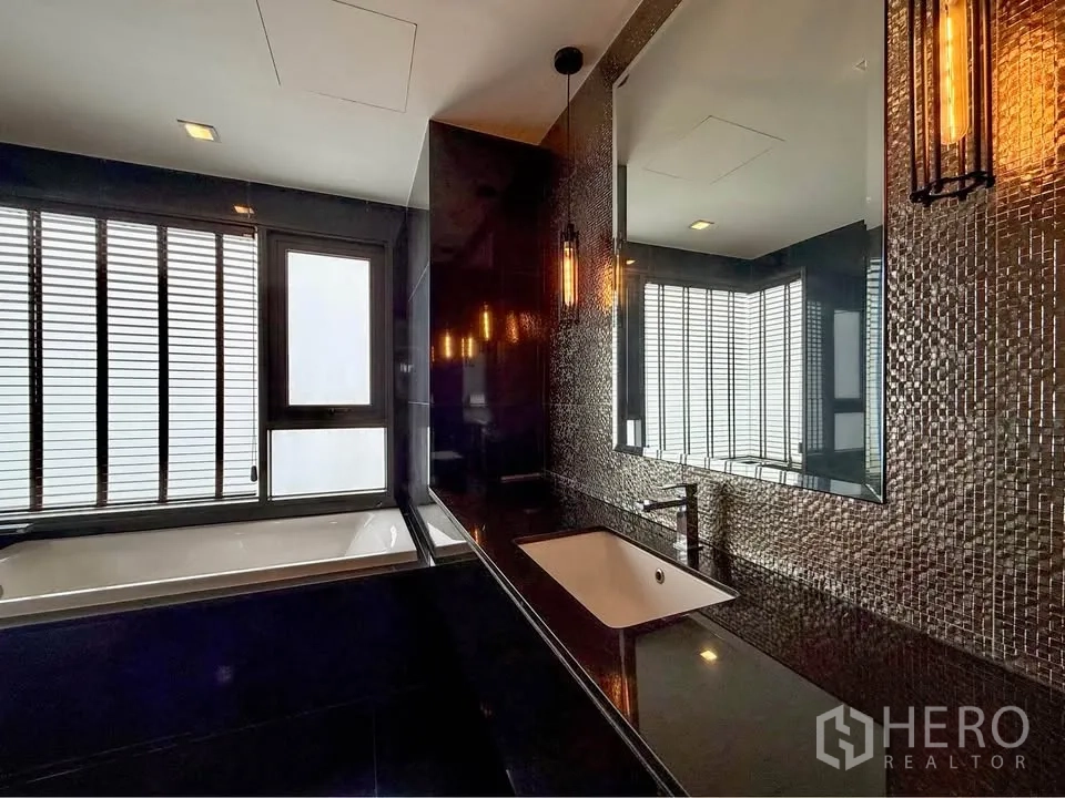 Condominium for rent in Khlong Toei, Bangkok - Bathroom vanity with mosaic wall tiles, mirror and view to bathtub and windows.