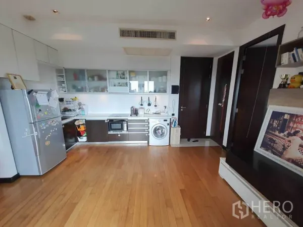 Condominium for rent in Yan Nawa, Bangkok - Open-plan kitchen with white cabinetry, built-in hob, microwave, washing machine and wood floors.