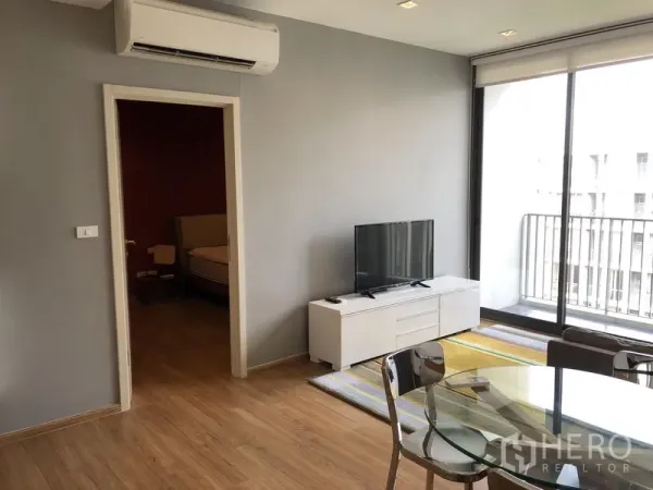 Condominium for rent in Watthana, Bangkok - Living area with wall-mounted air conditioner, TV unit and sliding glass doors to a compact balcony.