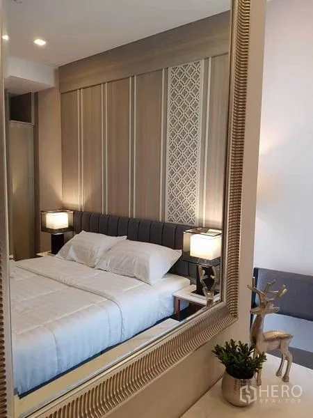 คอนโด ให้เช่าในWatthana, Bangkok - ภาพสะท้อนห้องนอนในกระจก หัวเตียงบุนุ่มและโคมไฟข้างเตียง พร้อมผนังลายตกแต่ง