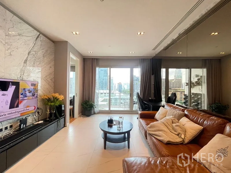 Condominium for rent in Pathum Wan, Bangkok - Open living area with balcony doors, mirrored wall and sectional leather sofa.