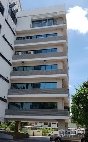 办公空间 出租在Khlong Toei, Bangkok - 中高层办公楼外立面，层叠阳台与蓝色玻璃窗，在晴空下位于คลองเตย。