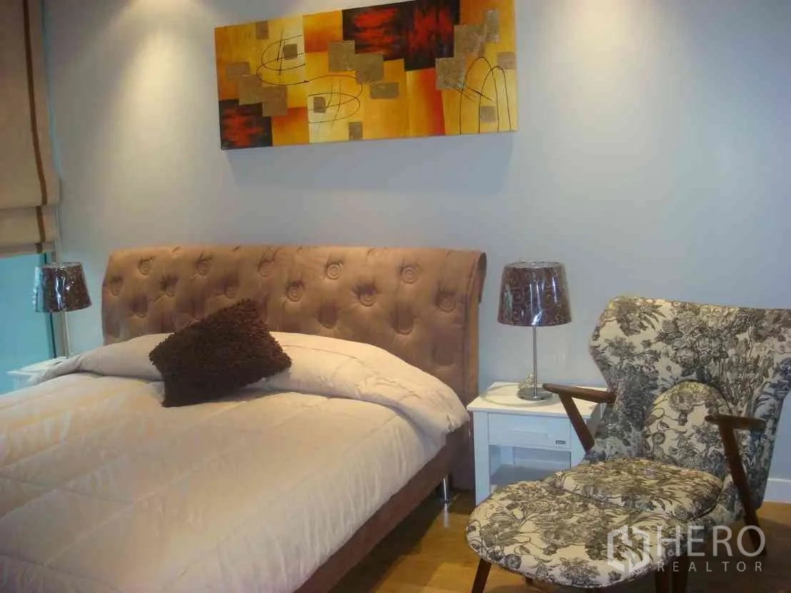 Condominium for rent in Watthana, Bangkok - Cozy bedroom with tufted headboard, bedside tables and a patterned lounge chair.