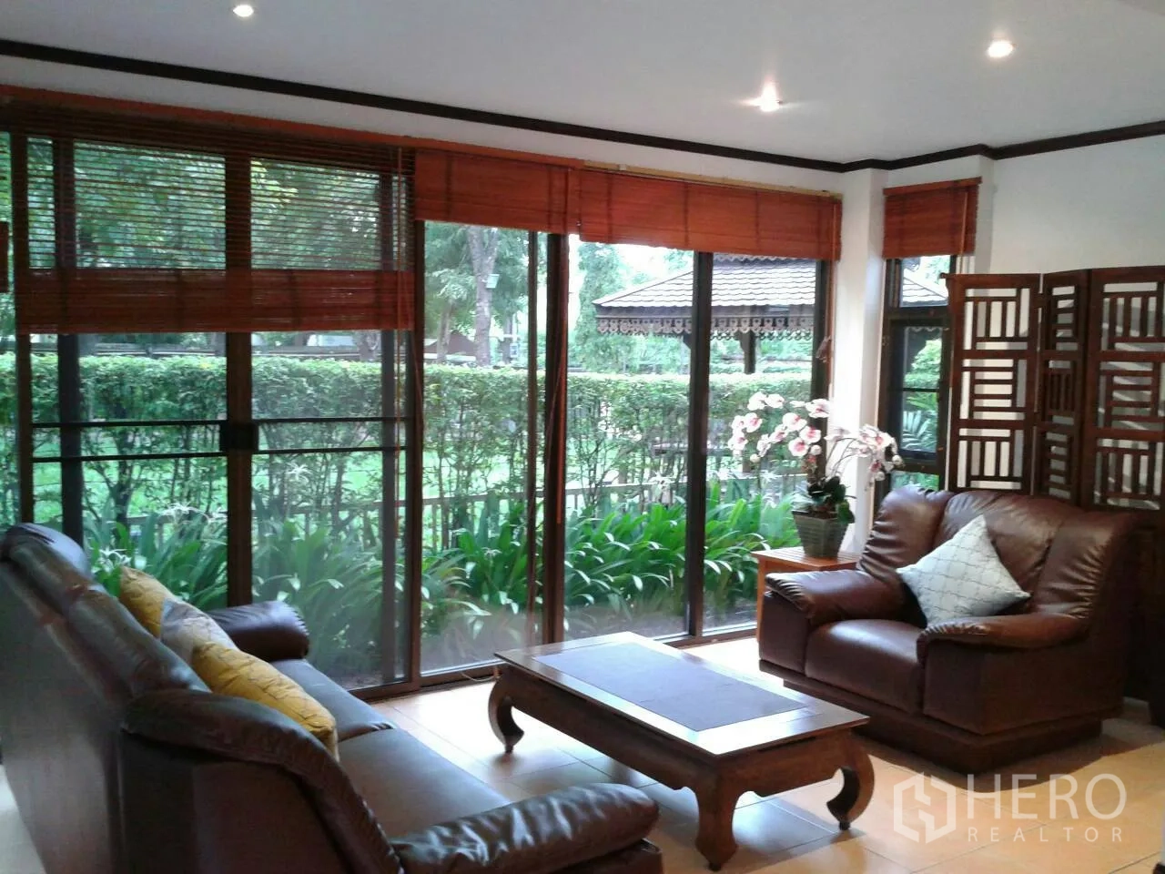Detached House for rent in Suan Luang, Bangkok - Bright living room with leather sofas and floor-to-ceiling windows overlooking a landscaped garden.