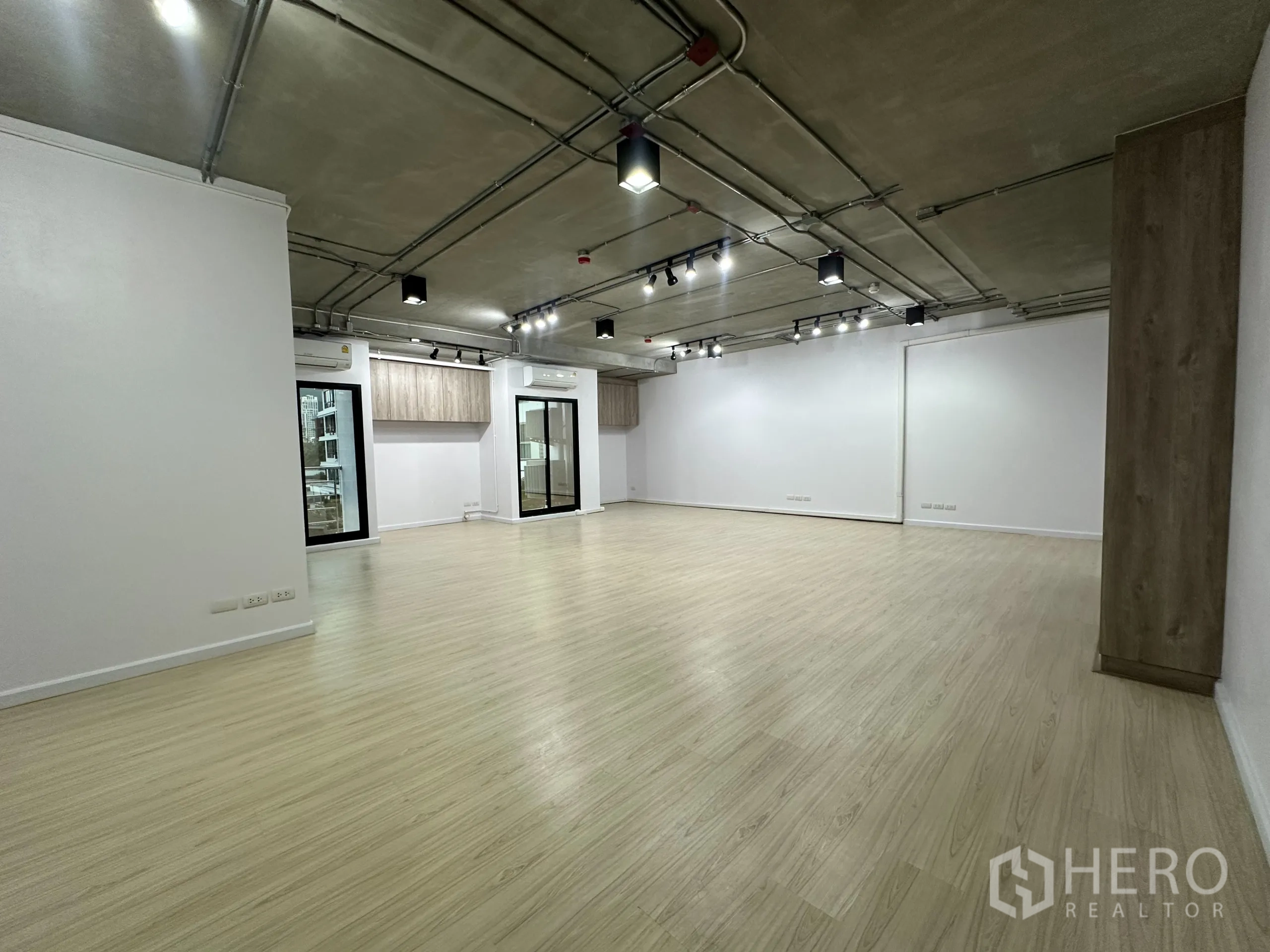 Office Space for rent in Watthana, Bangkok - Open-plan office with light wood flooring, exposed ceiling, track lighting, sliding glass doors and wall cabinets.
