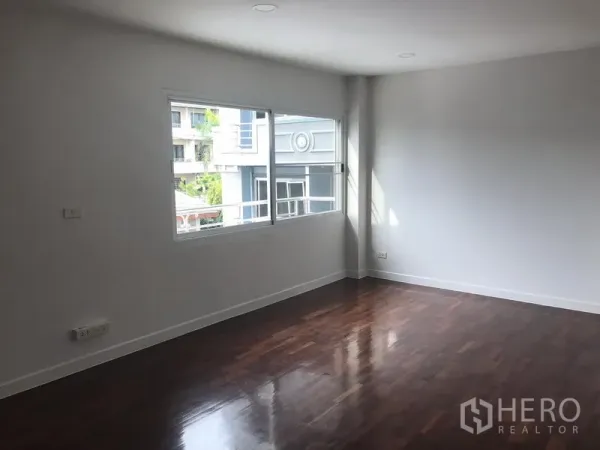 Home Office for rent or sale in Watthana, Bangkok - Sunlit office room with polished wood flooring and a wide corner window overlooking nearby buildings.