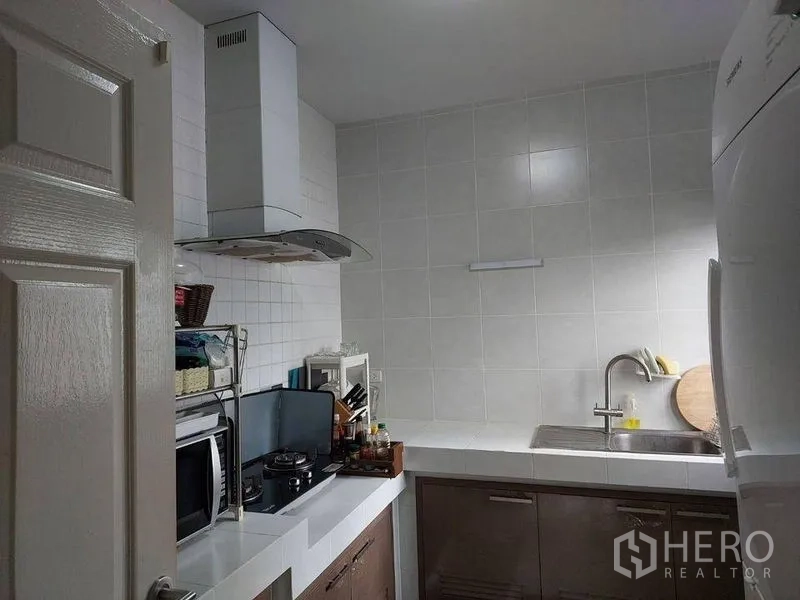 Detached House for sale in Khlong Sam Wa, Bangkok - Compact Thai kitchen with white countertop, cooktop, range hood, and sink.
