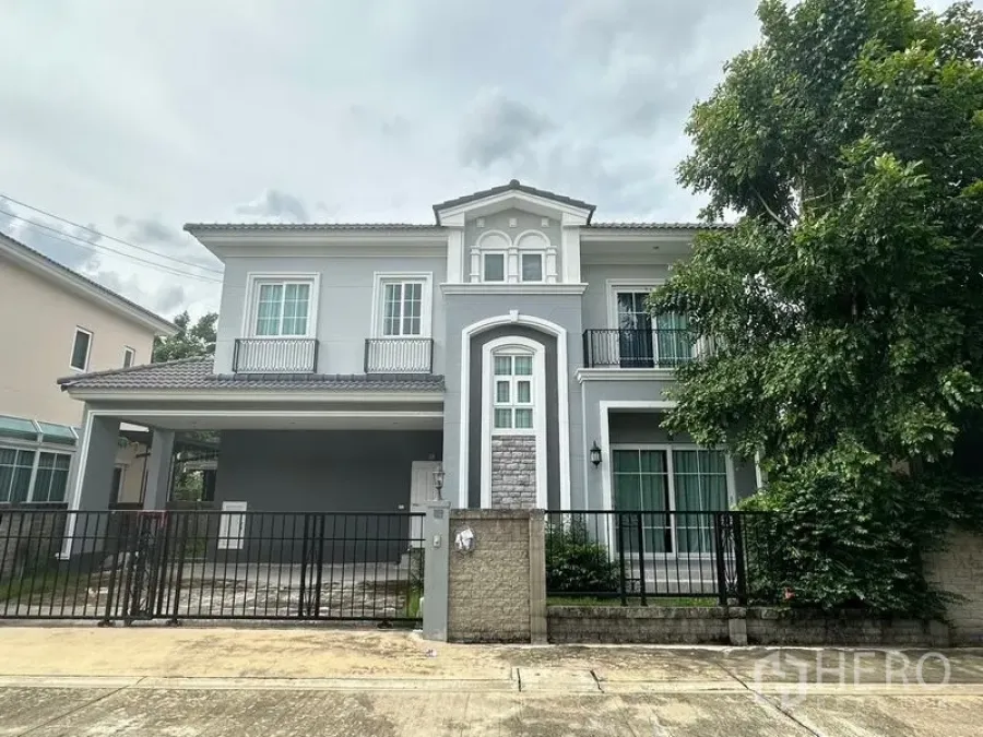 Detached House for sale in Bang Khen, Bangkok - Another front view of the grey two-storey house with fence and mature tree.