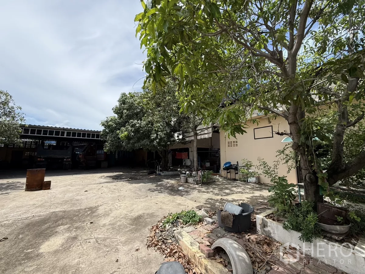 Warehouse for sale in Phra Samut Chedi, Samut Prakan - Paved yard with garden trees and a single‑storey outbuilding at the rear.