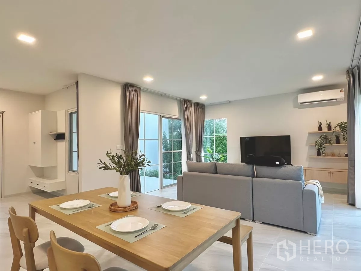 独立式住宅 出租在Bang Phli, Samut Prakan - 四人餐桌面向电视墙与置物架，窗外可见花园景观。