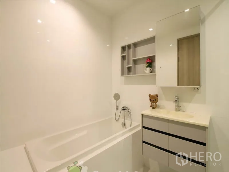 Condominium for rent or sale in Khlong Toei, Bangkok - Clean white bathroom featuring bathtub, handheld shower and vanity with storage.