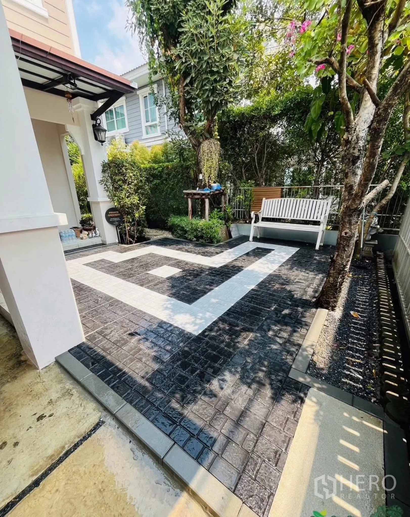Townhouse for rent or sale in Sai Mai, Bangkok - Front patio with patterned paving, trees and a white garden bench.