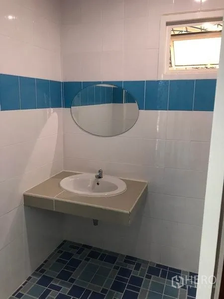 Factory for rent in Samut Prakan - Clean tiled washroom with countertop basin, round mirror and blue accent tiles.
