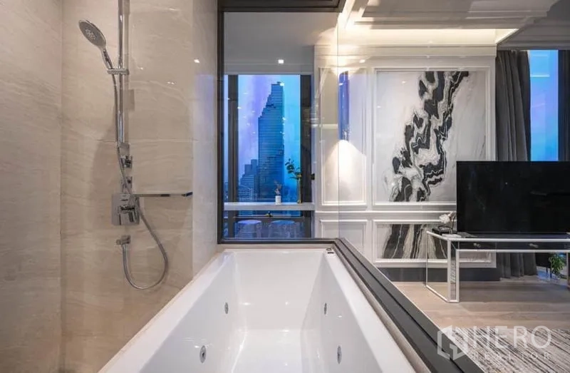 Condominium for rent in Bang Rak, Bangkok - Evening view from the bathroom with tub and glass wall toward a marble-accent living room.