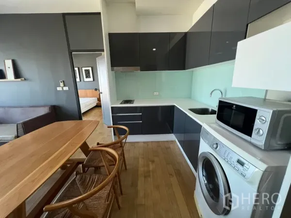 Condominium for rent or sale in Watthana, Bangkok - Open-plan kitchen with glossy cabinets, glass backsplash, dining table, microwave and washing machine