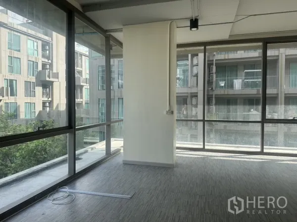 办公空间 出租在Phra Khanong, Bangkok - 转角工作区，环绕玻璃与中央立柱，可见周边住宅楼景。