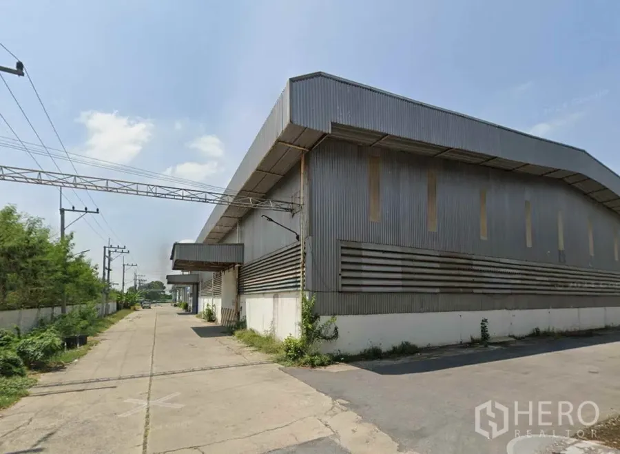 Warehouse for rent in Nong Khae, Saraburi - Exterior of a metal-clad warehouse in Nong Khae, Saraburi with covered loading bays and a wide concrete truck lane.