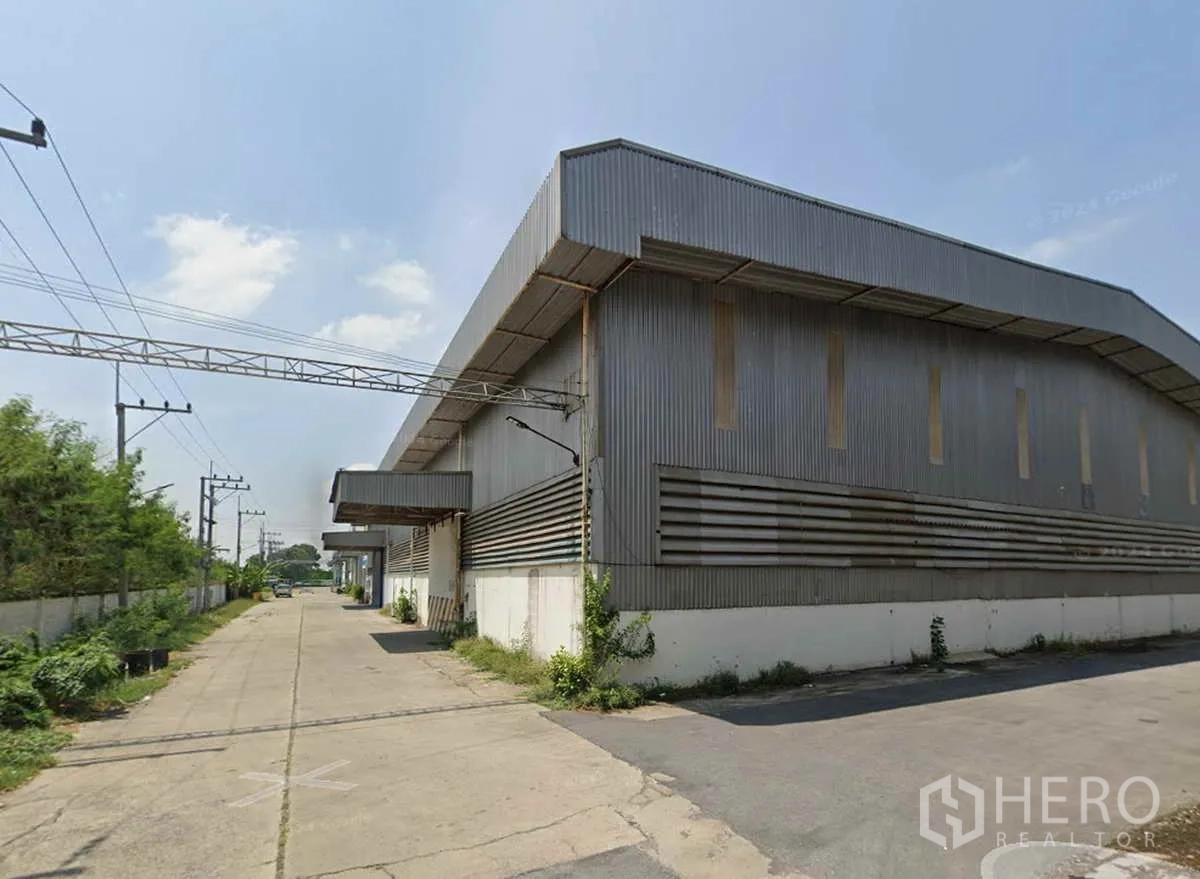 Warehouse for rent in Nong Khae, Saraburi - Exterior of a metal-clad warehouse in Nong Khae, Saraburi with covered loading bays and a wide concrete truck lane.