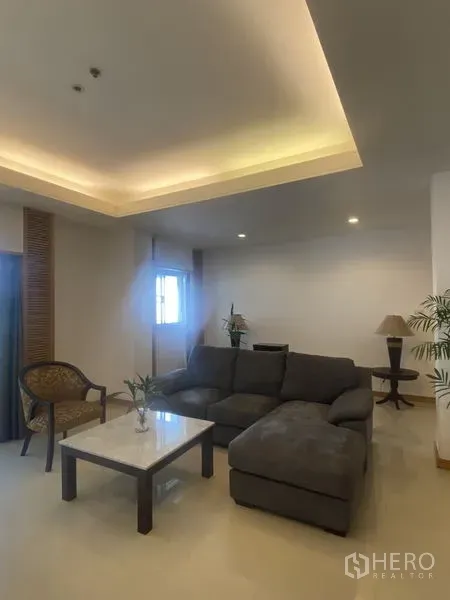 Condominium for rent - Living room with L-shaped gray sofa, marble coffee table, armchair and cove-lit ceiling.