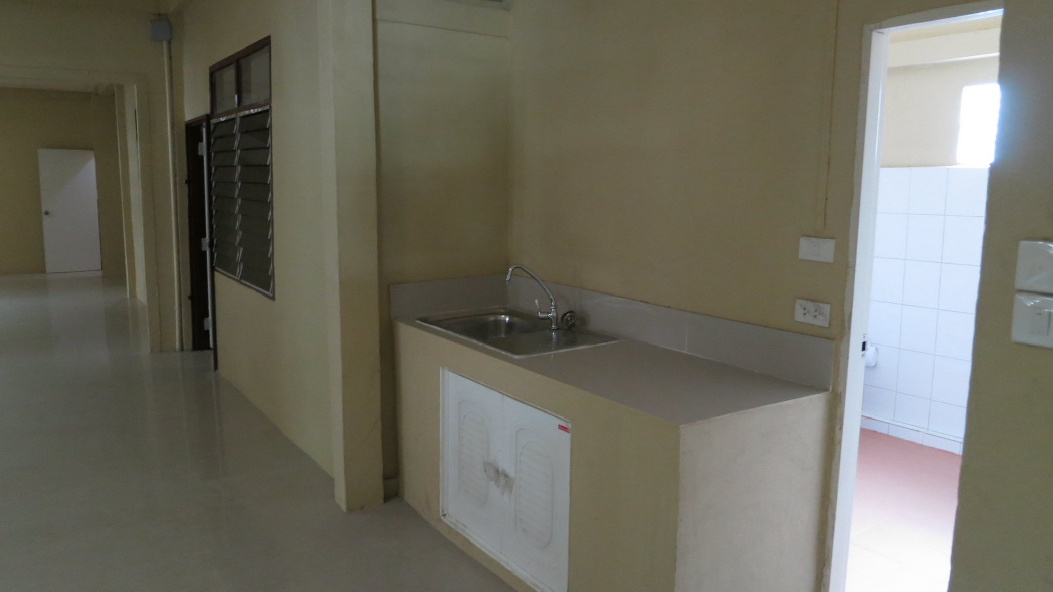 Warehouse for rent in Wang Thonglang, Bangkok - Small pantry counter with sink beside a tiled restroom and louvered window.