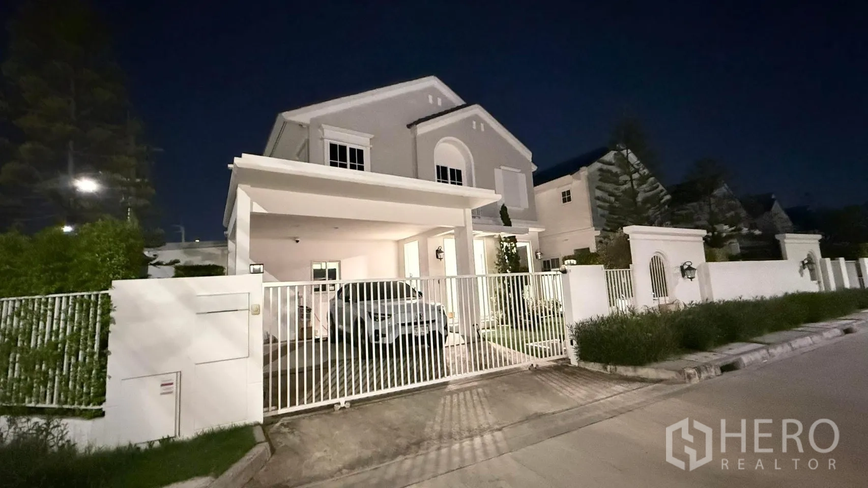 Detached House for rent or sale in Bang Phli, Samut Prakan - Two-storey detached house at night with white gate, covered carport, and driveway.