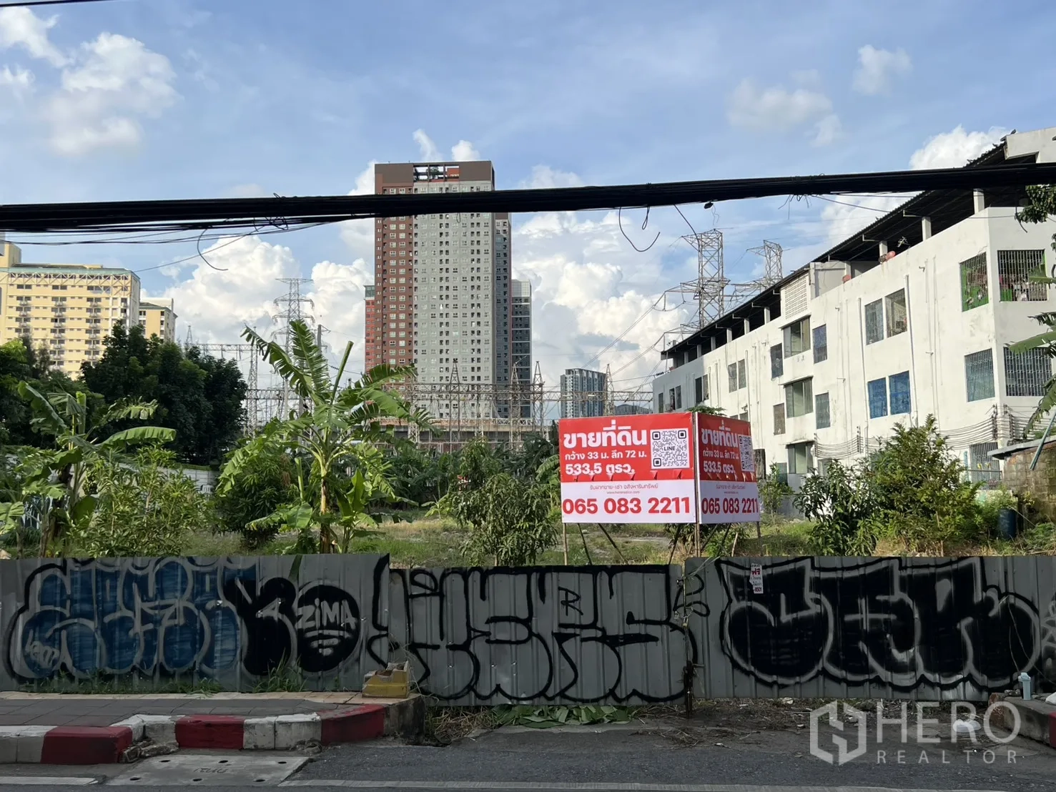 ที่ดิน ขายในSuan Luang, Bangkok - มุมมองด้านหน้าแปลงจากถนน มีกำแพงกราฟฟิตีและป้ายขาย เห็นเส้นขอบฟ้าเมือง