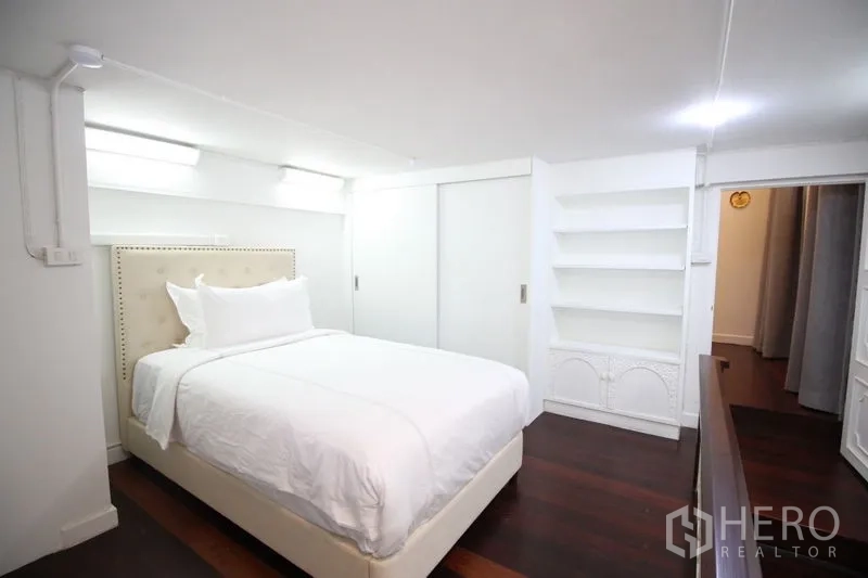 Detached House for rent in Chatuchak, Bangkok - Compact guest bedroom with white walls, built‑in shelving, sliding closet doors, and dark wood floors.