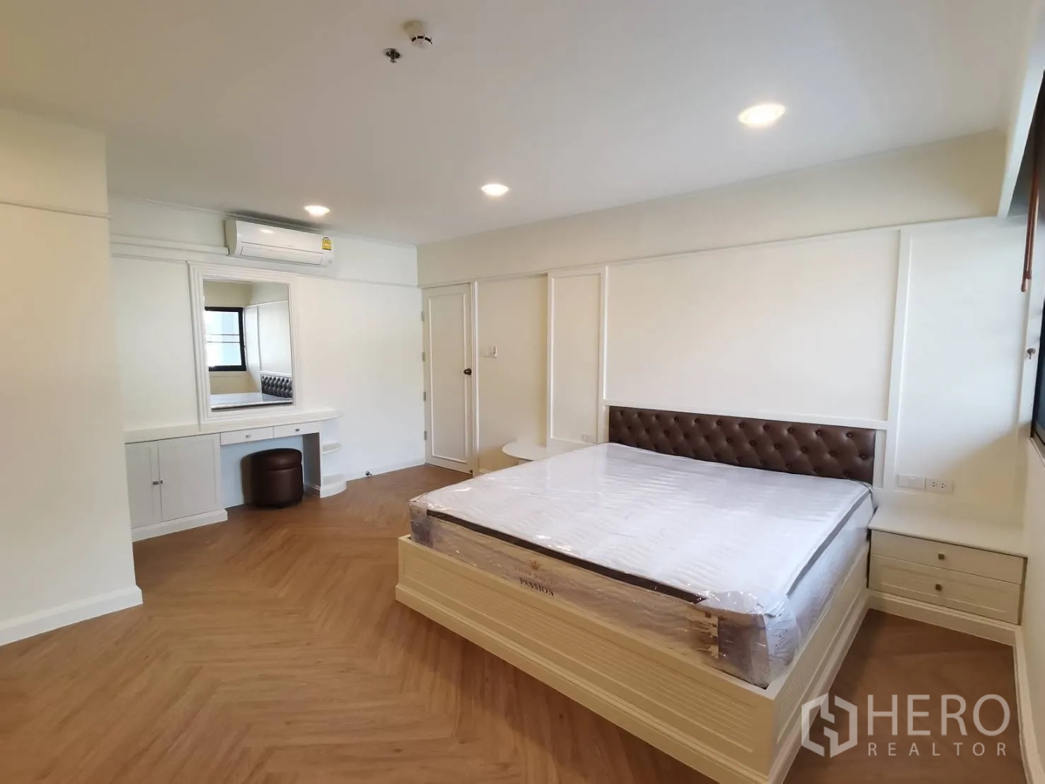 Condominium for rent in Watthana, Bangkok - Bedroom with tufted headboard, dressing table, and wood-look flooring.