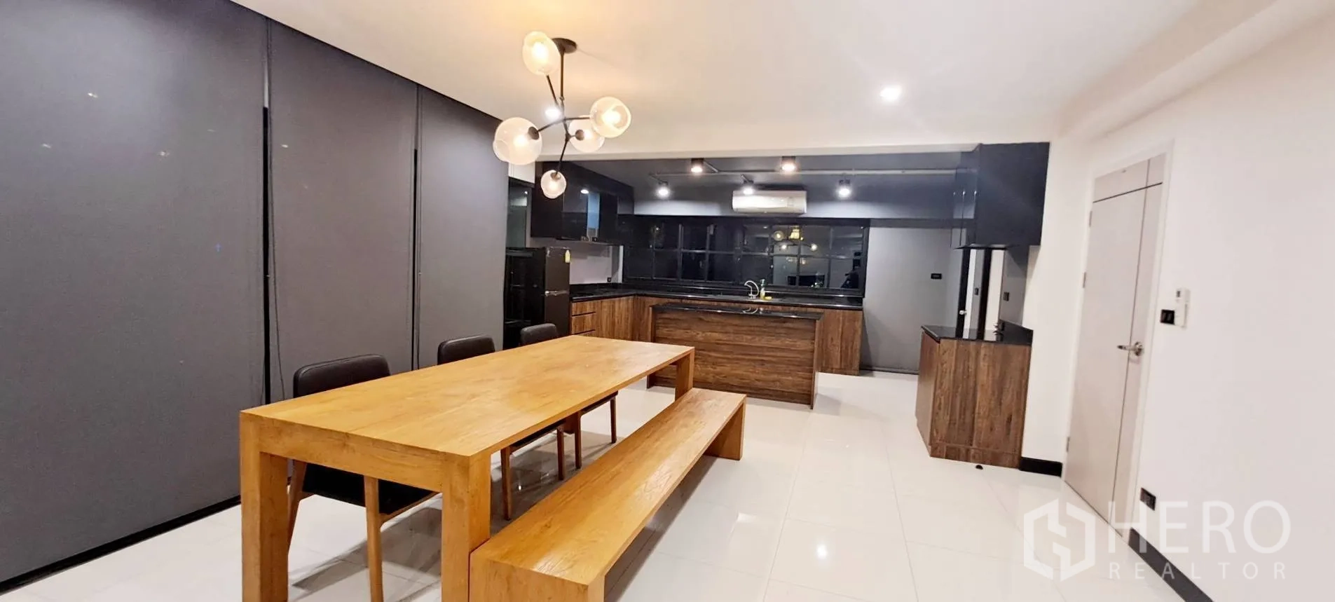 Apartment for rent in Phra Khanong, Bangkok - Dining zone with long wooden table and bench beside a modern kitchen.