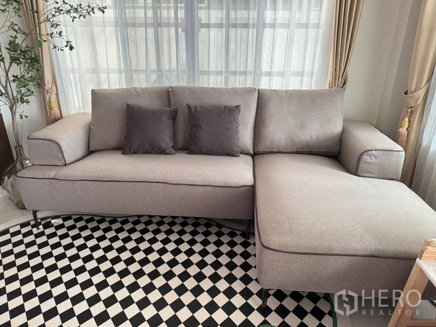 บ้าน ให้เช่าในMueang Samut Prakan, Samut Prakan - ห้องนั่งเล่นสว่าง โซฟาแอลสีเทา พรมลายตาราง และผ้าม่านโปร่ง