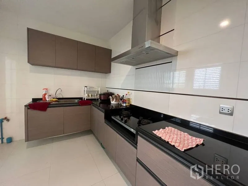 Detached House for rent or sale in Bang Phli, Samut Prakan - Modern L-shaped kitchen with black stone countertops, gas hobs and stainless hood.