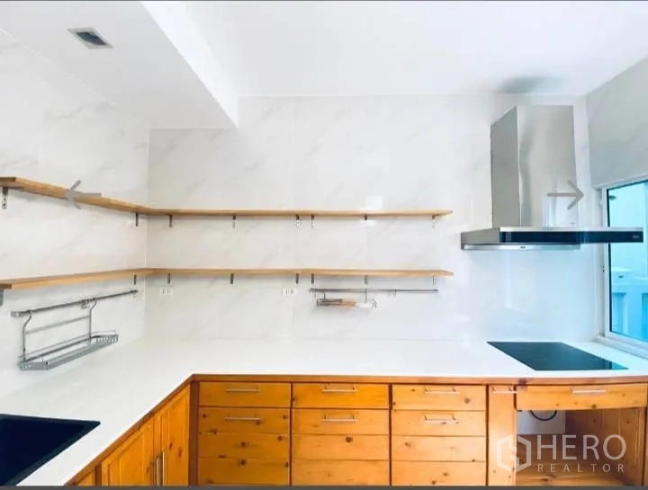 Detached House for sale in Saphan Sung, Bangkok - U-shaped kitchen with electric cooktop, stainless hood and open wooden shelves.