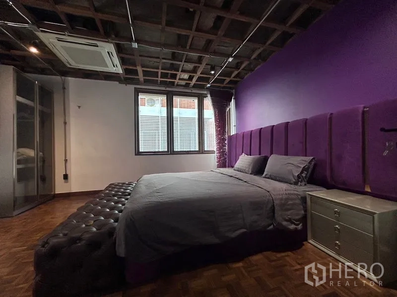 Apartment for rent in Khlong Toei, Bangkok - Bedroom with purple feature wall and upholstered headboard, large windows and ceiling-mounted AC.