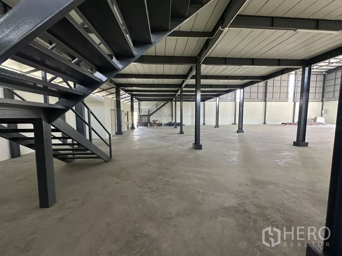 货栈 出租在Prawet, Bangkok - 夹层下方视角，钢楼梯与立柱，地面空间通透。