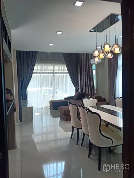 Detached House for rent in Thanyaburi, Pathum Thani - Open-plan living and dining area with pendant lights, sofa seating, sheer curtains, and glossy tile floors.