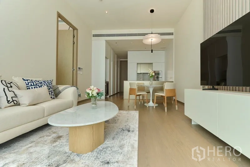 Condominium for rent in Pathum Wan, Bangkok - Spacious living room with sofa, TV console and a clear view toward the sleek kitchen.