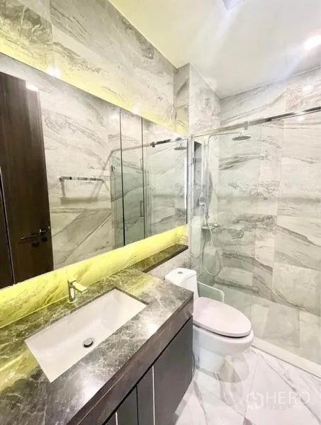 Condominium for rent in Watthana, Bangkok - Second marble bathroom with backlit mirror, vanity and glass shower.