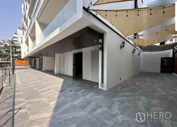 零售空间 出租 - 瓦他那区现代商业体内的宽阔石材露台，配有遮阳帆和敞开的店面入口。