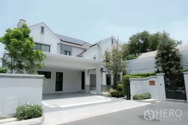 Detached House for rent or sale in Saphan Sung, Bangkok - Front exterior of white detached house with landscaped greenery and a wide driveway.