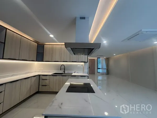 Townhouse for rent in Watthana, Bangkok - Kitchen island with induction cooktop and range hood overlooking open living area.